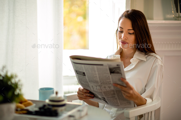 Young woman reading newspaper while having morning coffee at home Stock  Photo by nd3000